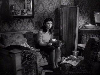 Movie still from “Obsession” (1943), directed by Luchino Visconti – A woman sitting on a couch holding a coffee mug; Medium shot, High angle