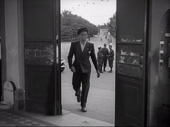 Movie still from “Obsession” (1943), directed by Luchino Visconti – A man in a suit walking through an open door; Wide shot, Low angle