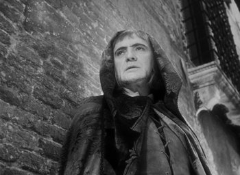 Movie still from “Othello” (1951), directed by Orson Welles – Black and white photograph of a man wearing a hooded cloak; Close Up shot, Low angle