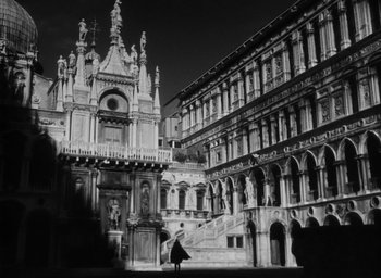 Movie still from “Othello” (1951), directed by Orson Welles – A black - and - white photo of a person walking in front of a building; Extreme Wide shot, Low angle