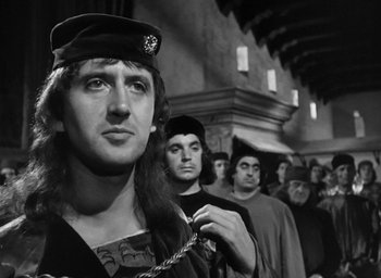 Movie still from “Othello” (1951), directed by Orson Welles – A group of men standing next to each other in front of a building; Close Up shot, Over the shoulder angle