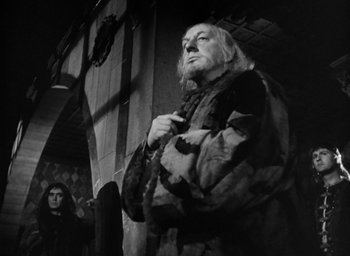 Movie still from “Othello” (1951), directed by Orson Welles – An old man standing next to a woman in front of a building; Medium shot, Low angle