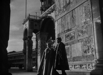 Movie still from “Othello” (1951), directed by Orson Welles – Two men are standing in front of a building; Wide shot, Low angle