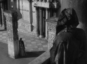 Movie still from “Othello” (1951), directed by Orson Welles – A man standing in front of a statue in a building; Wide shot, High angle