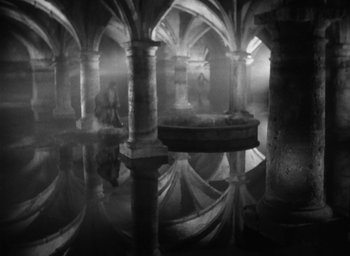 Movie still from “Othello” (1951), directed by Orson Welles – Two people are standing in a room with pillars; Extreme Wide shot, High angle