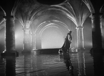 Movie still from “Othello” (1951), directed by Orson Welles – A man and a dog are standing in the water; Extreme Wide shot, High angle