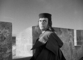 Movie still from “Othello” (1951), directed by Orson Welles – A man wearing a hat standing in front of a wall; Medium shot, Low angle