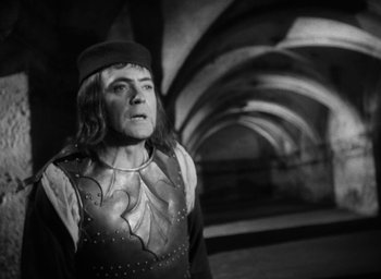 Movie still from “Othello” (1951), directed by Orson Welles – A man dressed as a medieval knight in a tunnel; Medium shot, Over the shoulder angle