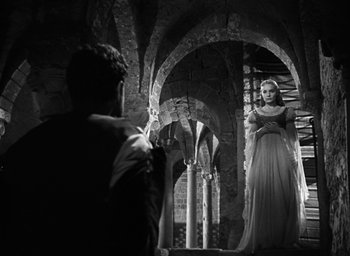 Movie still from “Othello” (1951), directed by Orson Welles – A woman in a white dress standing in front of a man; Wide shot, Over the shoulder angle