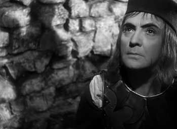 Movie still from “Othello” (1951), directed by Orson Welles – A man with long black hair wearing a hat and holding an object; Close Up shot, High angle