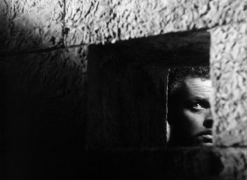 Movie still from “Othello” (1951), directed by Orson Welles – A black and white photo of a man looking through a window; Close Up shot, Low angle