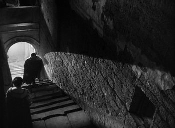 Movie still from “Othello” (1951), directed by Orson Welles – A man walking down a set of stairs in a tunnel; Wide shot, Low angle