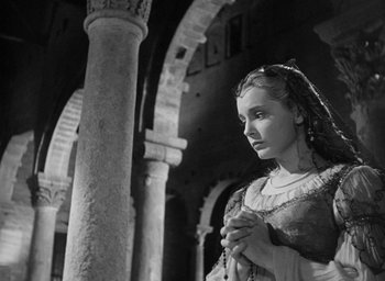 Movie still from “Othello” (1951), directed by Orson Welles – A black and white photo of a woman holding a rosary; Medium shot, Low angle