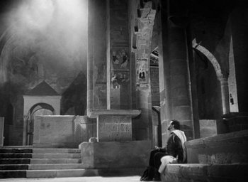 Movie still from “Othello” (1951), directed by Orson Welles – A man sitting on steps in front of a building; Extreme Wide shot, High angle