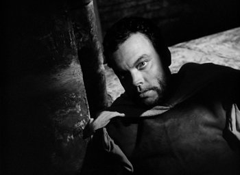 Movie still from “Othello” (1951), directed by Orson Welles – Black and white photograph of a man leaning against a pole; Close Up shot, High angle