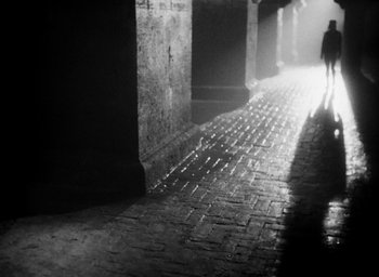 Movie still from “Othello” (1951), directed by Orson Welles – A person is walking down a brick walkway; Wide shot, Low angle