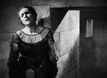 Movie still from “Othello” (1951), directed by Orson Welles – An older woman wearing a dress and a chain; Medium shot, Low angle