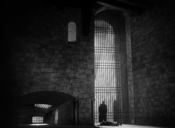 Movie still from “Othello” (1951), directed by Orson Welles – A man standing in front of a window with bars; Extreme Wide shot, Low angle