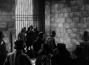 Movie still from “Othello” (1951), directed by Orson Welles – A group of people standing in front of a brick wall; Wide shot, High angle