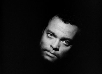 Movie still from “Othello” (1951), directed by Orson Welles – Black and white photograph of a man's face in the dark; Close Up shot, Overhead angle