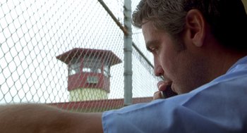 Movie still from “Out of Sight” (1998), directed by Steven Soderbergh – A man in a blue shirt is talking on a cell phone in front of a fence; Close Up shot, Low angle