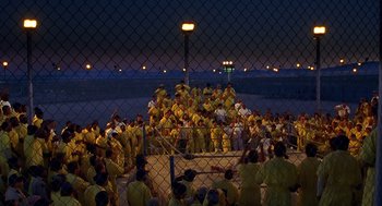 Movie still from “Out of Sight” (1998), directed by Steven Soderbergh – A large group of people in yellow suits standing in front of a fence; Extreme Wide shot, High angle