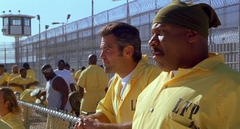 Movie still from “Out of Sight” (1998), directed by Steven Soderbergh – A couple of men are standing in front of a fence; Medium shot, Low angle