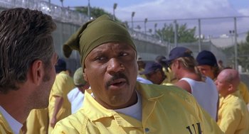 Movie still from “Out of Sight” (1998), directed by Steven Soderbergh – A man in a yellow shirt and a green hat is in front of a group of people; Close Up shot, Low angle