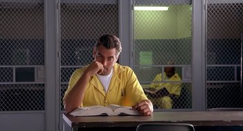 Movie still from “Out of Sight” (1998), directed by Steven Soderbergh – A man sitting at a table reading a book in a jail cell; Medium shot, Over the shoulder angle