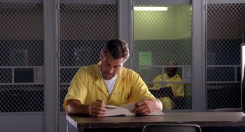 Movie still from “Out of Sight” (1998), directed by Steven Soderbergh – A man sitting at a table writing on a book; Medium shot, Low angle
