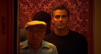 Movie still from “Out of Sight” (1998), directed by Steven Soderbergh – A man standing next to an older man in front of a wall; Medium shot, Low angle