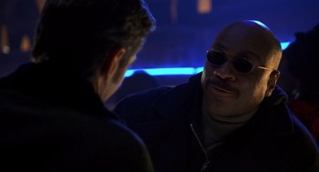 Movie still from “Out of Sight” (1998), directed by Steven Soderbergh – A man wearing sunglasses talking to another man in a dark room; Close Up shot, Over the shoulder angle