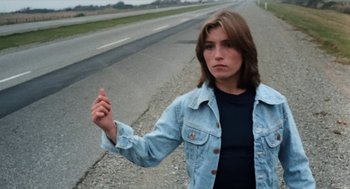 Movie still from “Out of the Blue” (1980), directed by Dennis Hopper – A woman in a jean jacket standing on the side of a road; Medium shot, High angle