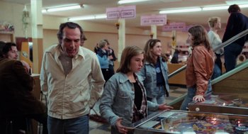 Movie still from “Out of the Blue” (1980), directed by Dennis Hopper – A group of people standing in a room looking at items; Medium shot, Over the shoulder angle