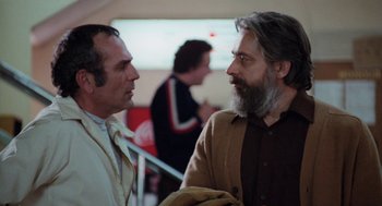 Movie still from “Out of the Blue” (1980), directed by Dennis Hopper – Two men talking to each other in front of a crowd; Medium shot, Over the shoulder angle