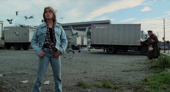 Movie still from “Out of the Blue” (1980), directed by Dennis Hopper – A woman standing in a parking lot next to a truck; Wide shot, Low angle
