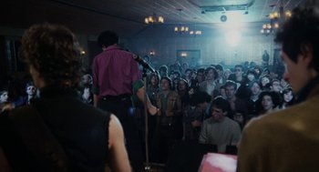 Movie still from “Out of the Blue” (1980), directed by Dennis Hopper – A group of people in a room with a microphone; Wide shot, Over the shoulder angle
