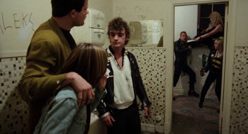 Movie still from “Out of the Blue” (1980), directed by Dennis Hopper – A group of people standing in a bathroom; Medium shot, Over the shoulder angle