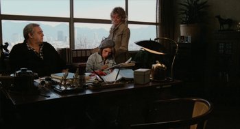 Movie still from “Out of the Blue” (1980), directed by Dennis Hopper – Two women sitting at a desk in front of a large window; Wide shot, High angle