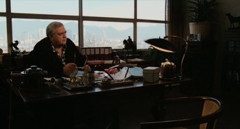 Movie still from “Out of the Blue” (1980), directed by Dennis Hopper – A man sitting at a desk in front of a large window; Wide shot, Low angle