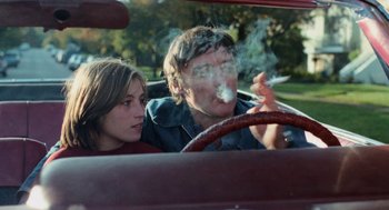 Movie still from “Out of the Blue” (1980), directed by Dennis Hopper – A man and a woman sitting in a car smoking; Medium shot, High angle