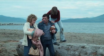 Movie still from “Out of the Blue” (1980), directed by Dennis Hopper – A man holding a football near two women on a beach; Medium shot, High angle
