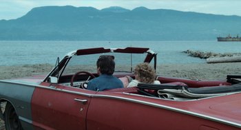 Movie still from “Out of the Blue” (1980), directed by Dennis Hopper – A man and a woman sitting in the back of a red car; Wide shot, High angle