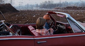 Movie still from “Out of the Blue” (1980), directed by Dennis Hopper – A man and a woman driving a red car; Wide shot, High angle