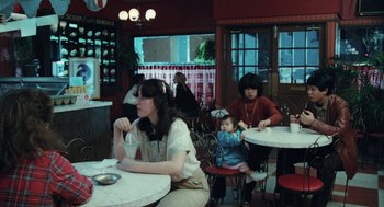 Movie still from “Out of the Blue” (1980), directed by Dennis Hopper – Two women and a child sitting at a table in a restaurant; Wide shot, High angle