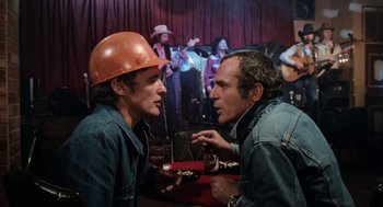 Movie still from “Out of the Blue” (1980), directed by Dennis Hopper – Two men in hard hats talking to each other; Medium shot, Over the shoulder angle