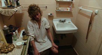 Movie still from “Out of the Blue” (1980), directed by Dennis Hopper – A woman sitting in a bathroom next to a white sink; Medium shot, High angle