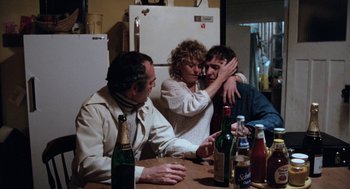 Movie still from “Out of the Blue” (1980), directed by Dennis Hopper – A group of people sitting at a table with bottles of alcohol; Medium shot, High angle