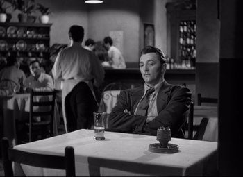 Movie still from “Out of the Past” (1947), directed by Jacques Tourneur – A black and white photo of a man sitting at a table; Medium shot, Over the shoulder angle