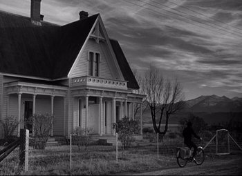 Movie still from “Out of the Past” (1947), directed by Jacques Tourneur – A person riding a bike in front of an old house; Extreme Wide shot, Low angle